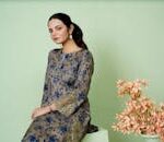 Young woman in floral embroidered dress posing with flowers indoors.